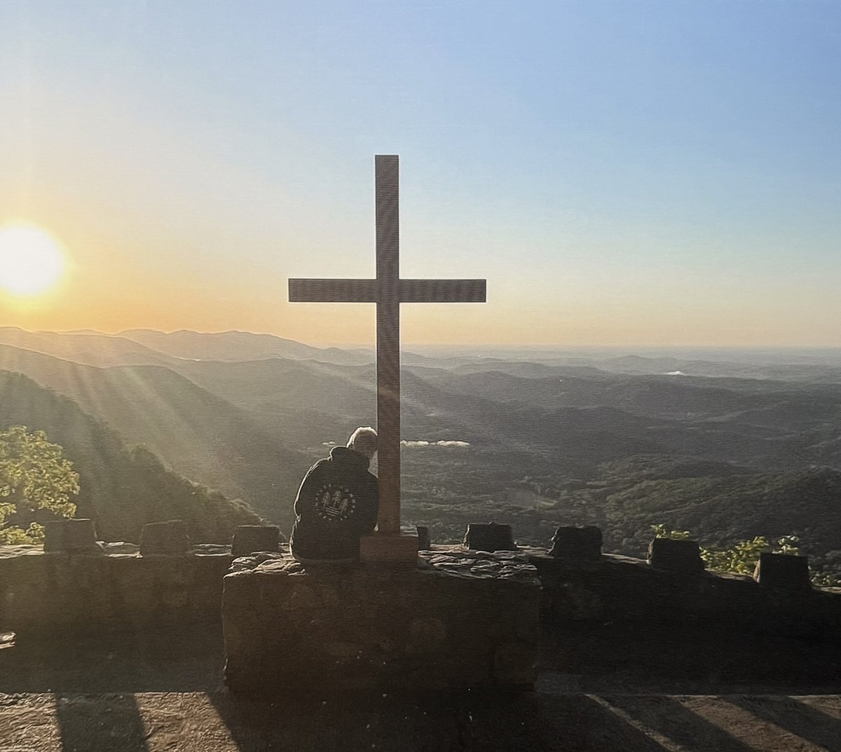 A cross silhouetted against a mountain sunrise — a reflection of Jodi's faith and The Climb